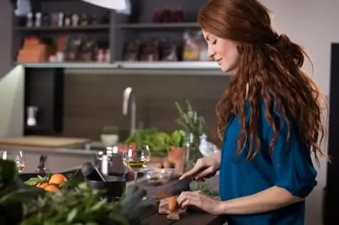 Happy young woman cutting carrots in kitchen. Happy woman cooking vegetables salad in kitchen.