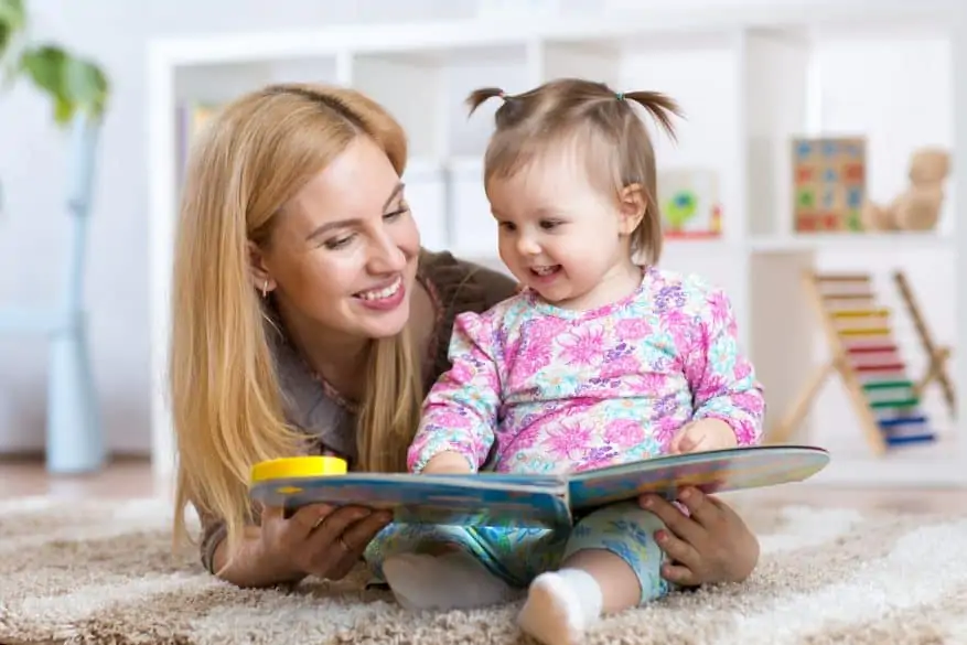 happy mother reading a book to child girl at nursery