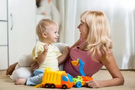 Smiling mother and child boy play with car toys together at home