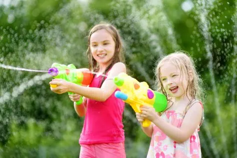 Adorable little girls playing with water guns on hot summer day.