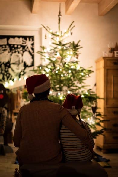 family Christmas traditions parent and child sitting in front of a Christmas tree
