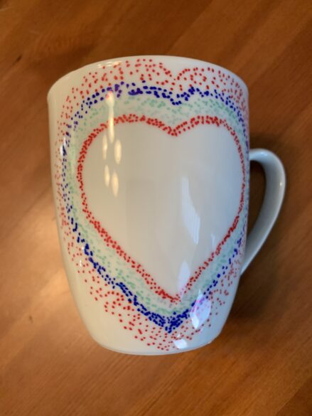 A mug with a heart shape and dots in different colors around it.