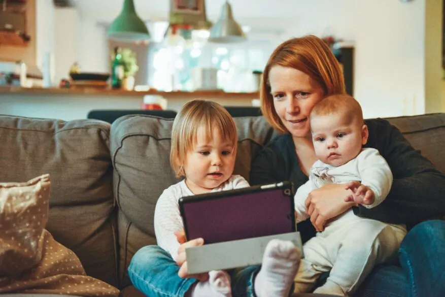 A mom sitting with 2 kids looking at a tablet.