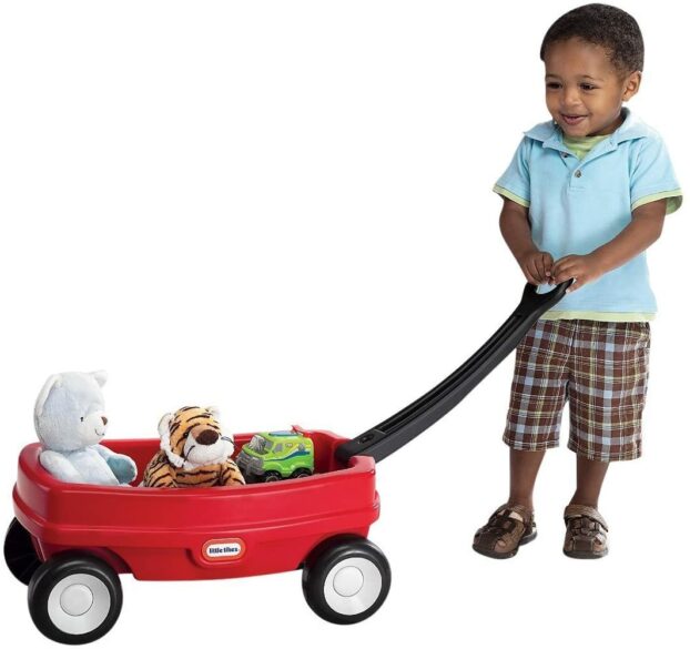 A boy pulling a red wagon with toys in it.