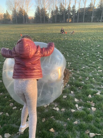 A girl pushing another girl who is in side of a bubble ball.