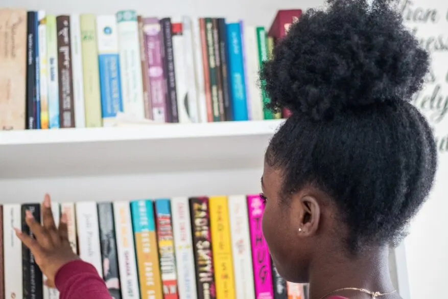 A girl picking a book from a shelf of books.