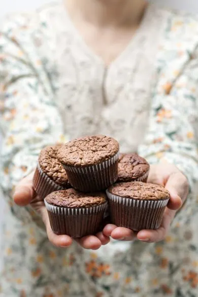 A person holding unfrosted chocolate cupcakes.