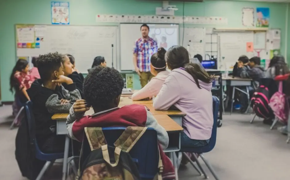 A classroom with the teacher at the front and kids sitting at desks.