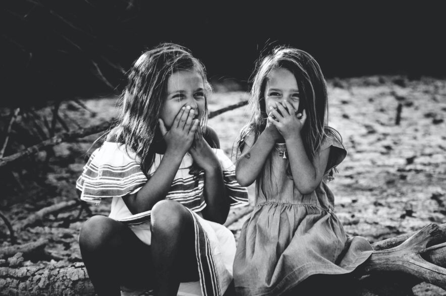 Two young girls laughing while covering their mouths with their hands.