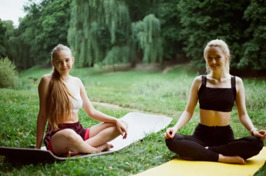 Two girls sitting on yoga mats outside.