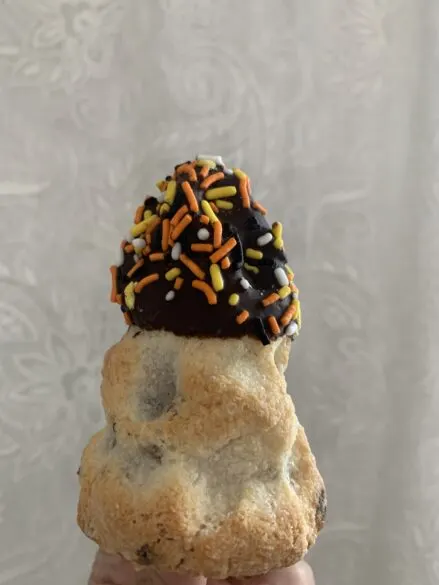 A Matterhorn Macaroon with chocolate on top and orange, white and yellow sprinkles.