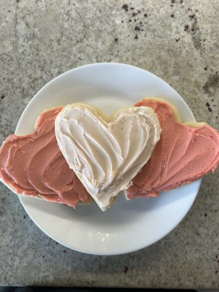 Three heart shaped frosted sugar cookies on a plate.