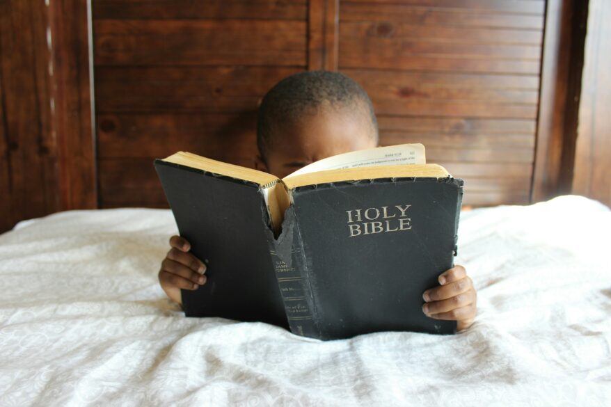 A child laying on a bed on their stomach with the Holy Bible open.