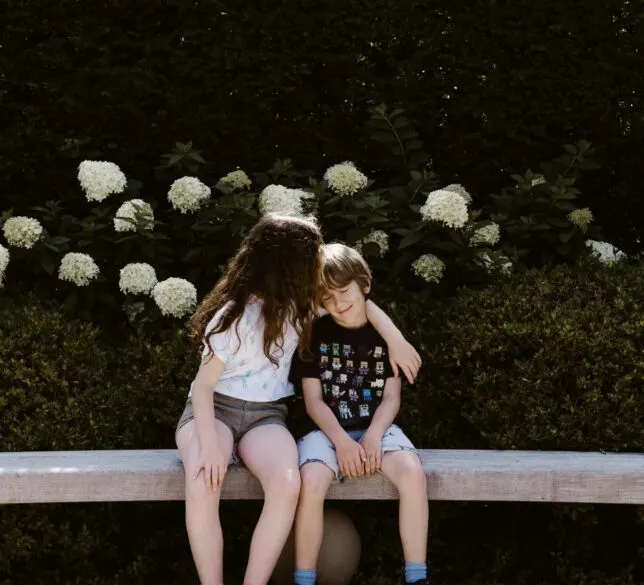 An older girl with her arm around a younger boy and kissing his head.