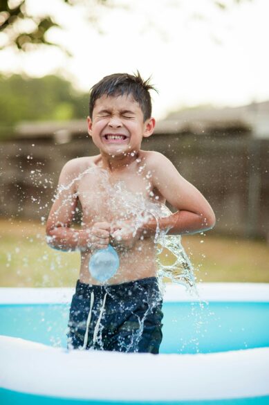 A boy holding a water balloon in an inflatable pool.